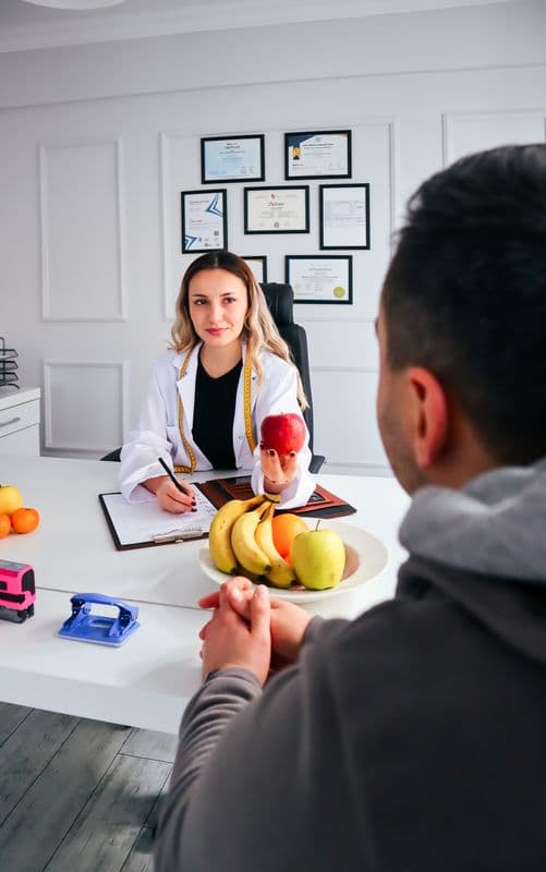 Nutricionista sorrindo e oferecendo uma maçã a um paciente durante consulta no consultório.