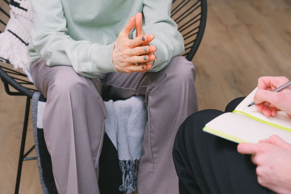 Psicoterapeuta fazendo anotações em um caderno durante uma sessão, com a paciente sentada à frente.